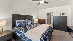 Een slaapkamer met een bed, nachtkastje, dressoir, plafondventilator en een deur naar een andere kamer.