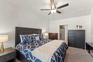 A bedroom with a bed, a nightstand, a dresser, a ceiling fan, and a door leading to another room. - The Gibraltar Retreat at Red Hawk (Las Cruces)