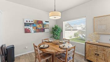A dining area with a wooden table, chairs, a hanging light fixture, and a window with blinds.