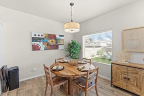 A dining area with a wooden table, chairs, a hanging light fixture, and a window with blinds. - The Gibraltar Retreat at Red Hawk (Las Cruces)