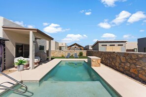 A swimming pool with a stone wall and a covered patio area.