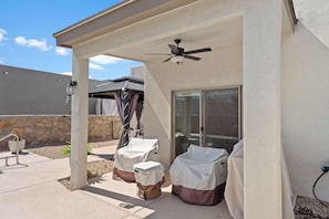 A covered patio area with a ceiling fan, two covered chairs, and a table.