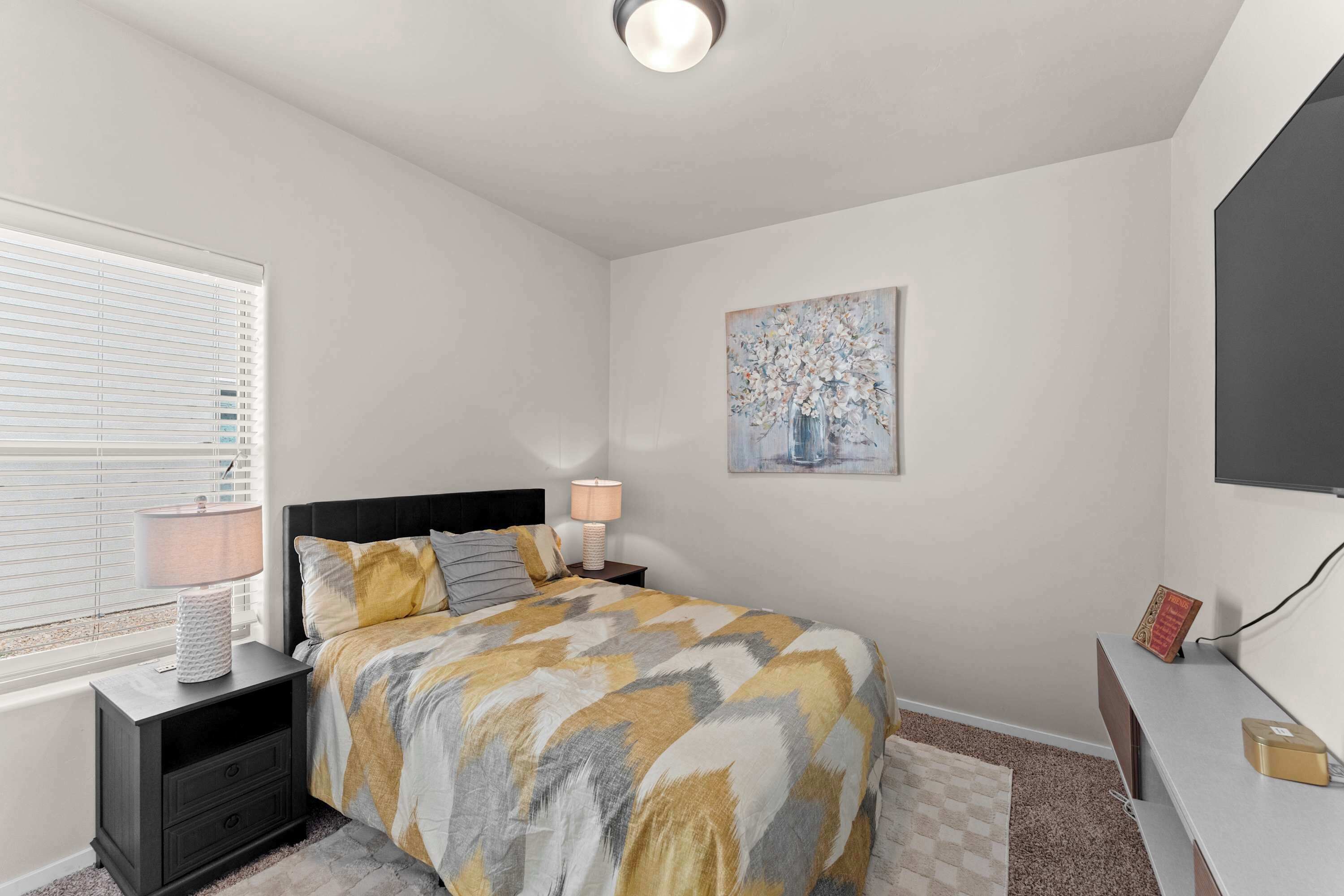 A bedroom with a bed, bedside tables, a lamp, a painting, and a television.