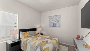 A bedroom with a bed, bedside tables, a lamp, a painting, and a television.