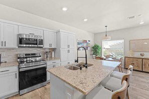 A modern kitchen with white cabinetry, stainless steel appliances, a granite countertop, and a dining area with a wooden table and chairs.