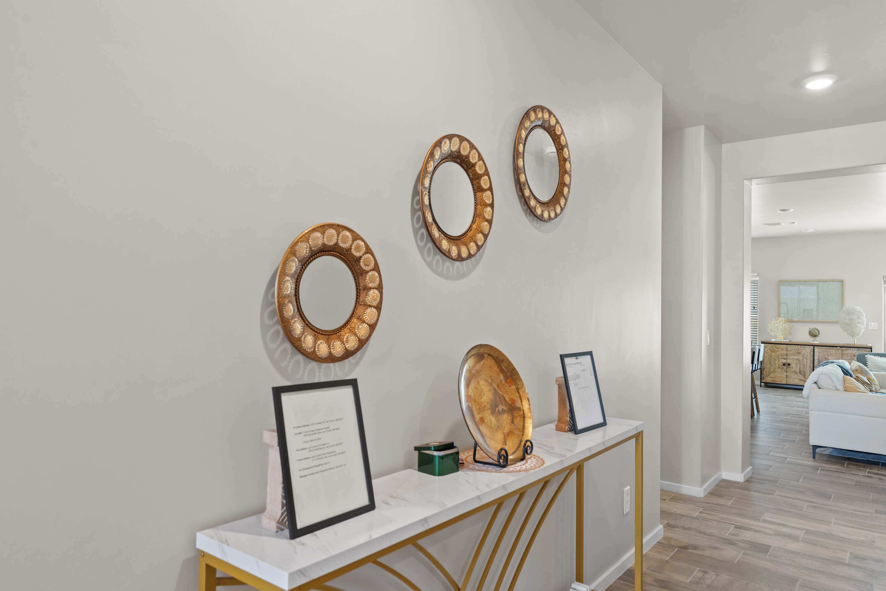 A modern interior with a white console table displaying framed certificates, a decorative mirror, and a wooden plate.