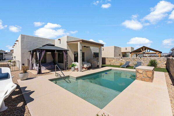 A pool area with a covered seating area, lounge chairs, and a stone wall.