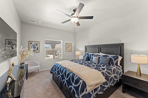 A bedroom with a bed, ceiling fan, bedside lamps, a chair, and artwork on the walls.