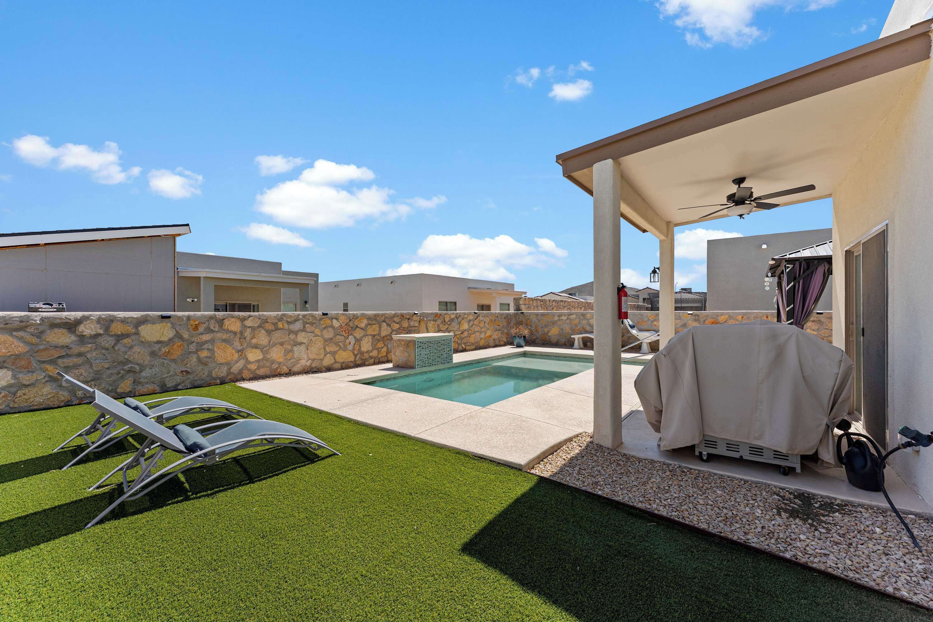 Un jardin avec une piscine, une pelouse artificielle et un espace patio couvert.