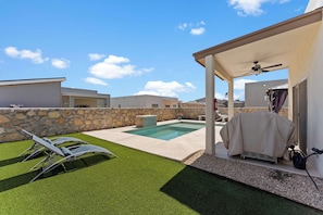 A backyard with a swimming pool, artificial grass, and a covered patio area.