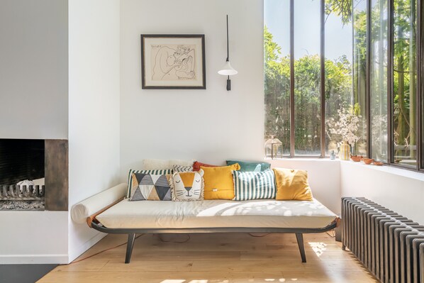 A modern living room with a sofa, a fireplace, a large window with a view of greenery, and a hanging light fixture. - Vrbo Property (Montreuil)