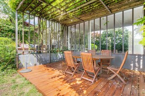 An outdoor patio with a wooden table and chairs, surrounded by a wooden deck and a pergola with vines. - Vrbo Property (Montreuil)