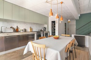 A modern kitchen with stainless steel appliances, a dining area with a table and chairs, and a staircase leading to an upper level. - Spacious architect-designed home, perfect for families—near Disneyland and Paris (Montreuil)
