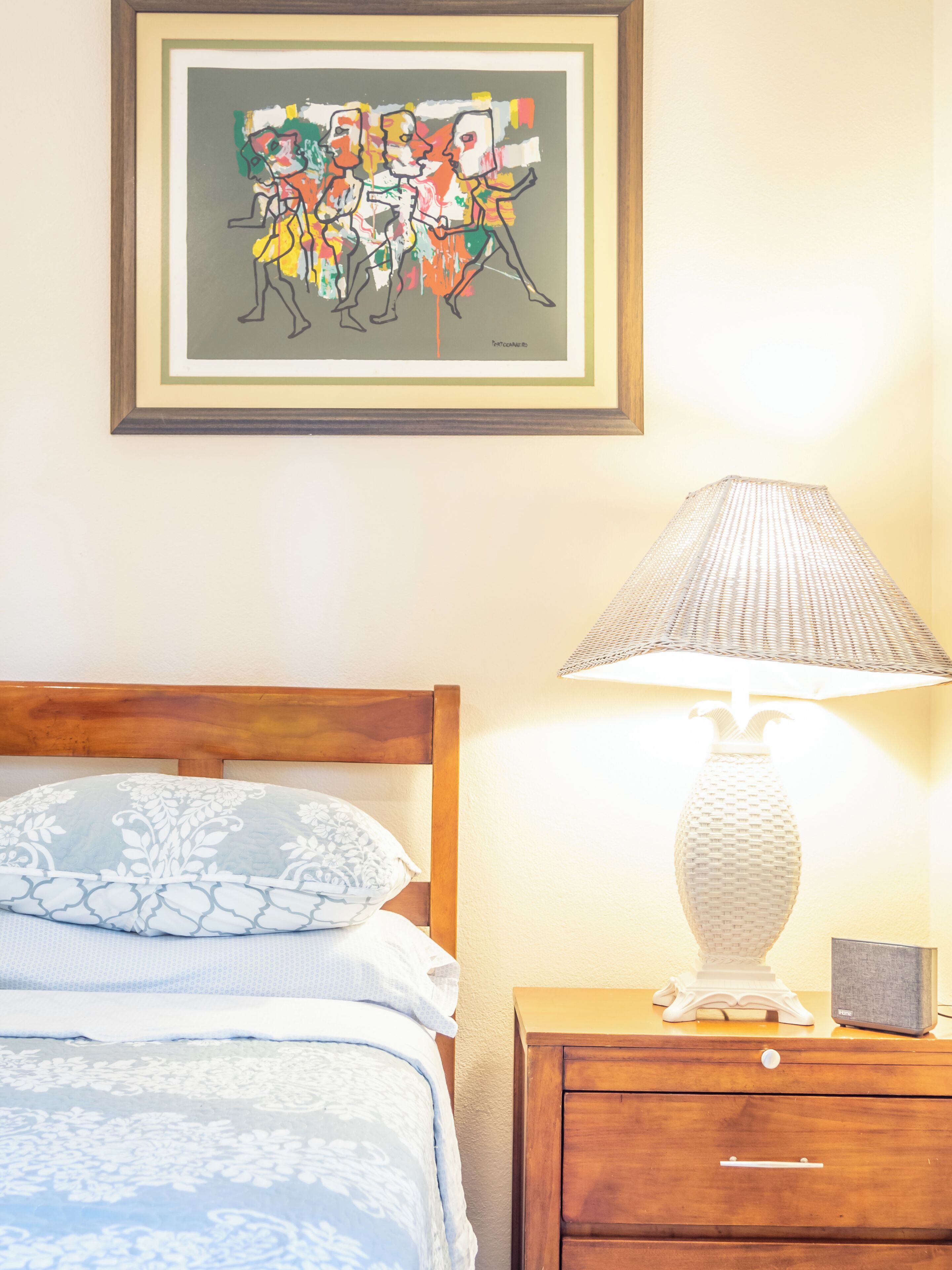 Une chambre à coucher avec un lit, une table de chevet avec une lampe et une œuvre d’art encadrée au mur.
