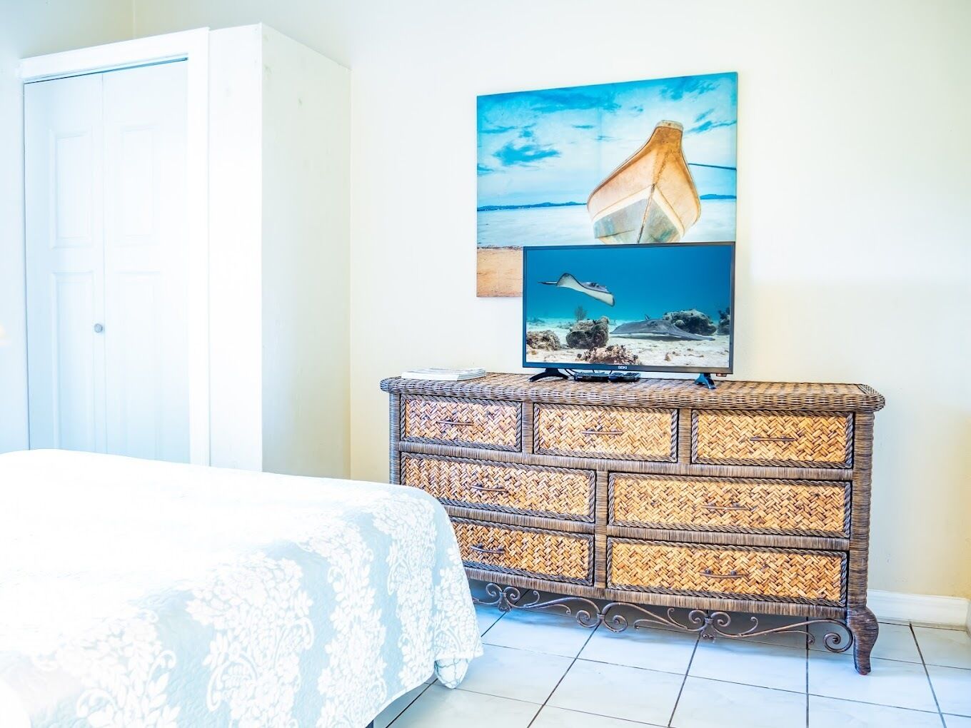 Une chambre à coucher avec un lit, une commode en osier et un téléviseur fixé au mur qui diffuse une scène sous-marine.