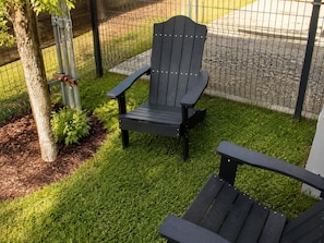 A black Adirondack chair in a grassy outdoor area with a metal fence in the background. - Modern Houston Retreat  Arcade • Patio • Stylish Stay (Houston)