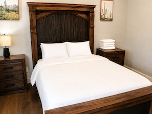A neatly made bed with white linens, a wooden headboard, a bedside table with a lamp, and a stack of towels. - Modern Houston Retreat  Arcade • Patio • Stylish Stay (Houston)