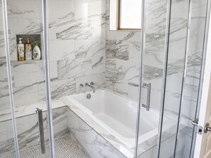Een moderne badkamer met een douchecabine van glas, een wit bad en een wand betegeld met marmer.