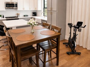 Een eetgedeelte met een houten tafel, vier stoelen, een koffiezetapparaat en een stilstaande hometrainer.