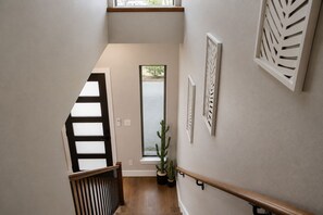 A staircase with a wooden handrail and a potted plant at the bottom. - Modern Houston Retreat  Arcade • Patio • Stylish Stay (Houston)