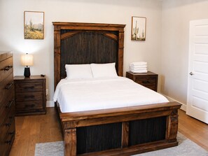 Een slaapkamer met een houten bed, een nachtkastje met een lamp, een dressoir en twee ingelijste foto's aan de muur.