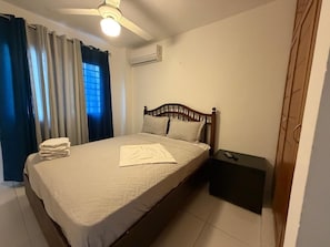 A bedroom with a bed, a bedside table, a ceiling fan, and an air conditioning unit. - Palma Real W (Santiago de los Caballeros)
