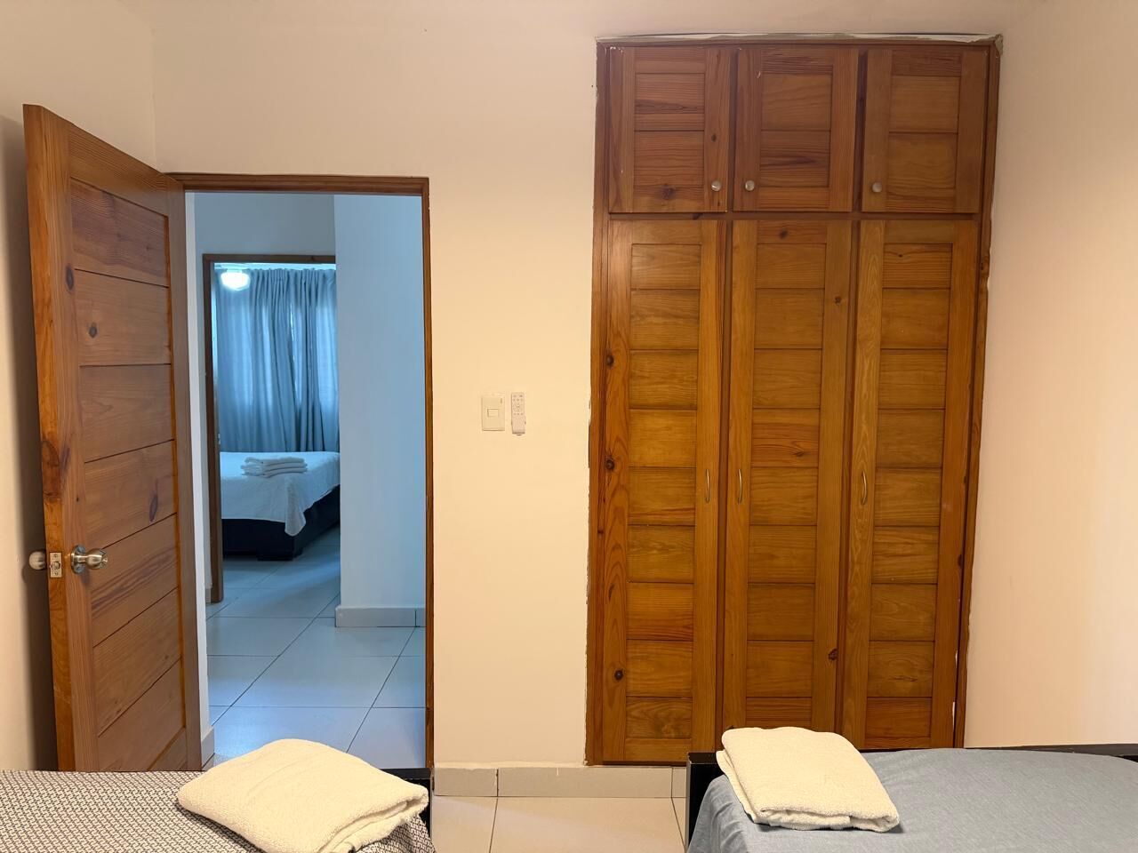 Ein Schlafzimmer mit einem Holzschrank, einem Bett mit weißer Daunendecke und einem durchgegangenen Tür angedeuteten Badezimmer.