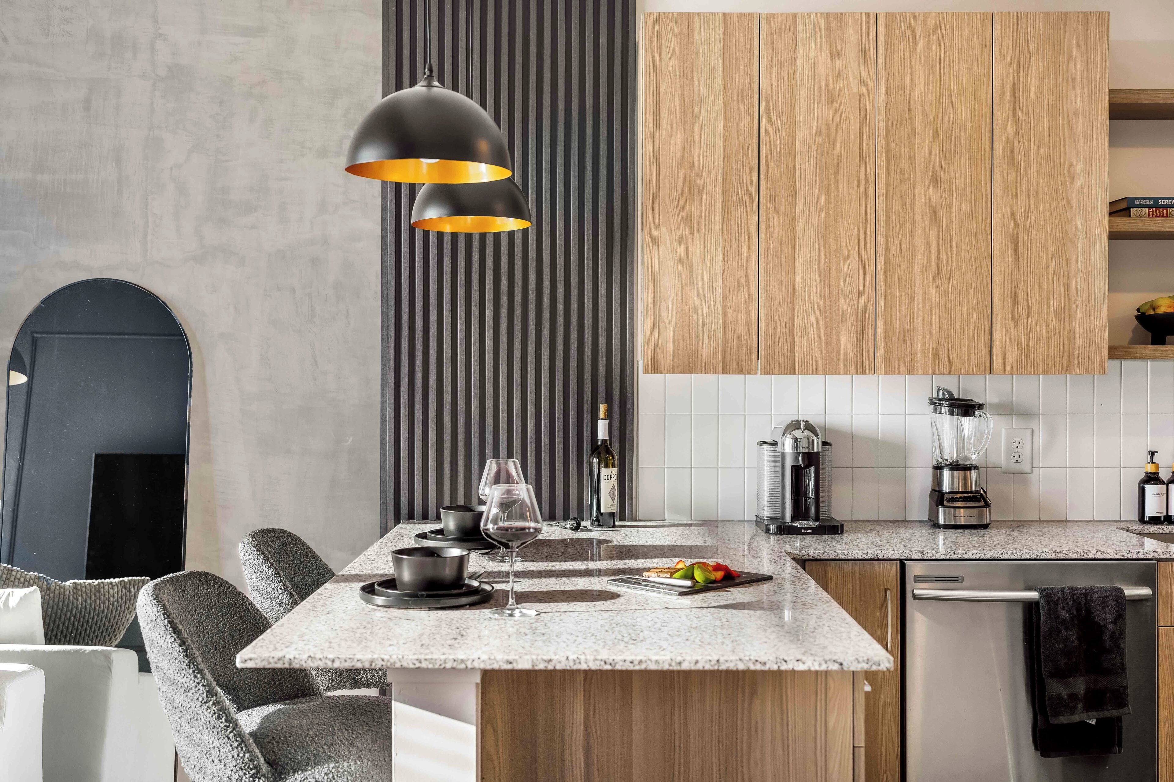 Eine moderne Küche mit einer zentralen Kochinsel, Holzschränken, einer schwarzen Pendelleuchte und einer gefliesten Rückwand.