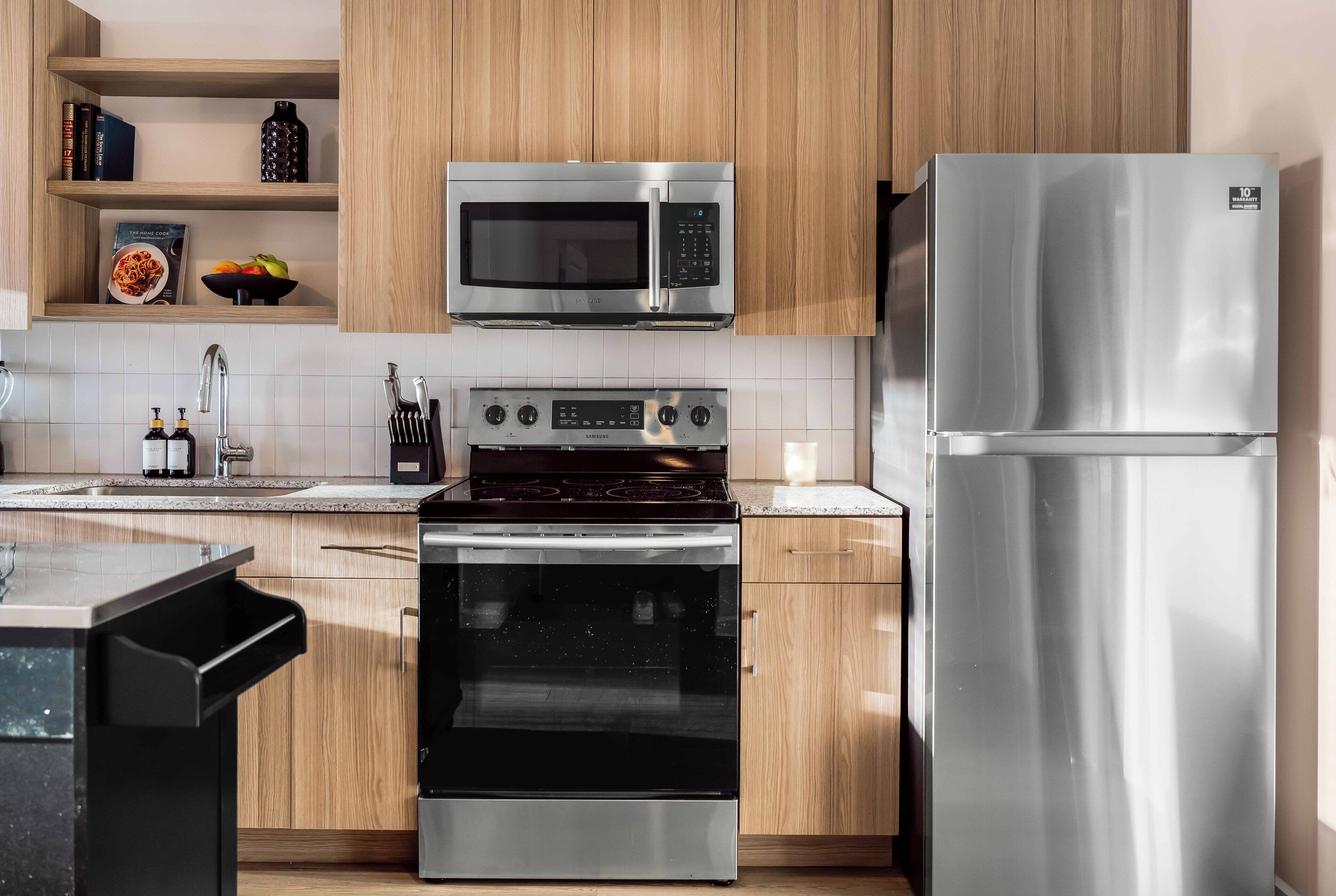A modern kitchen with stainless steel appliances, wooden cabinets, and a tiled backsplash.