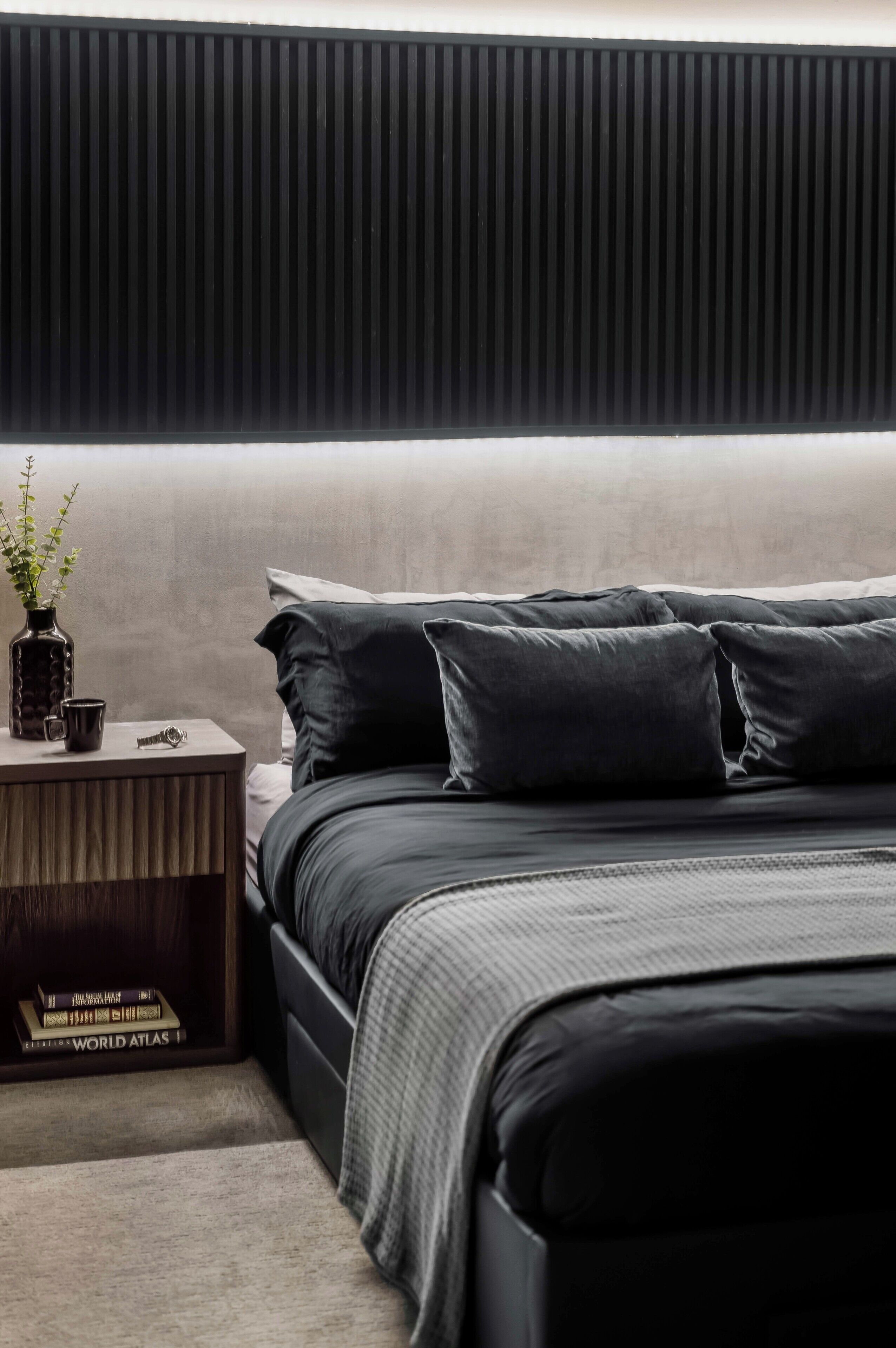 A modern bedroom with a bed, pillows, a nightstand, a vase with a plant, and books.