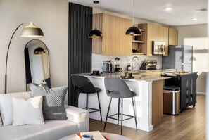 A modern kitchen with a central island, bar stools, a built-in oven, and a refrigerator. - The Dominic - 1BR Condo, King Bed, Pool, Gym (Orlando)