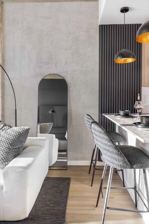 A modern kitchen with a bar area, a white sofa with grey cushions, and a dining table with bar stools. - The Dominic - 1BR Condo, King Bed, Pool, Gym (Orlando)