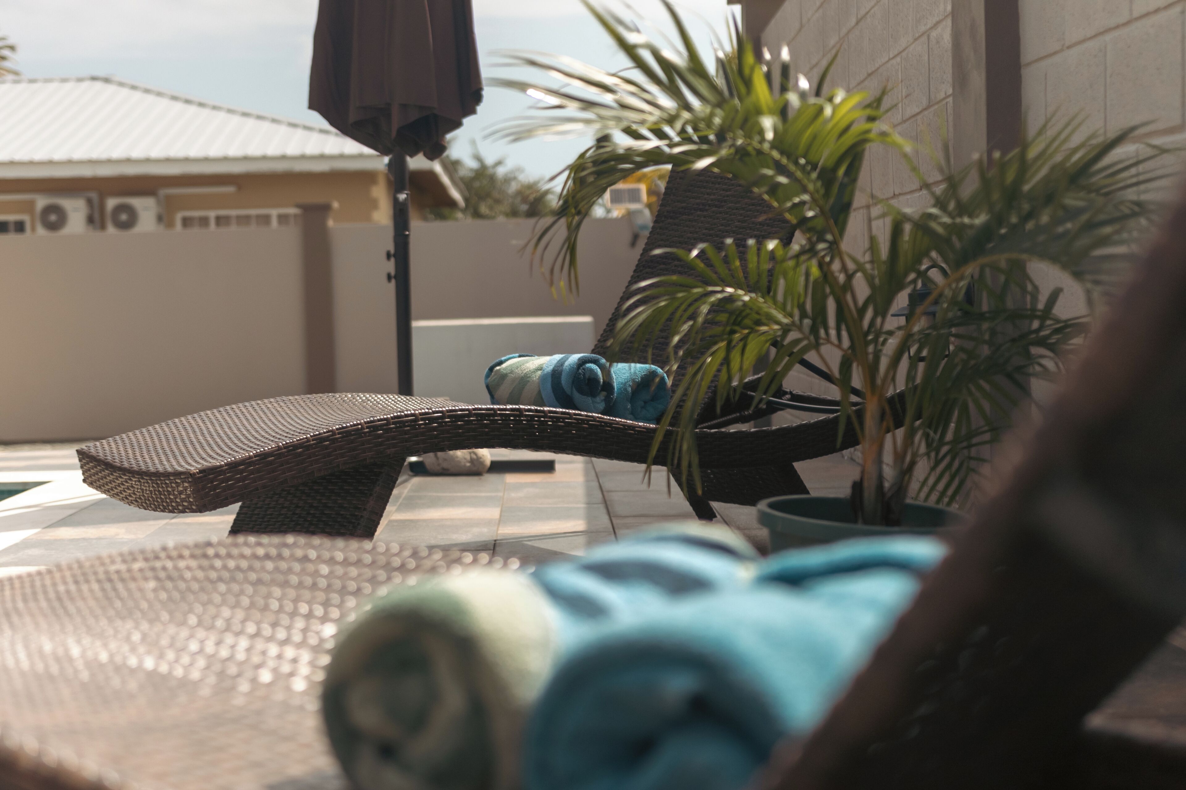 A sun lounger with a rolled towel, a small table, and a potted plant.
