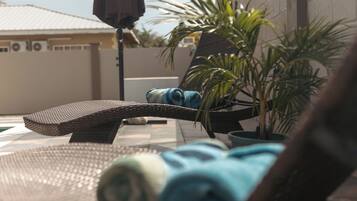 A sun lounger with a rolled towel, a small table, and a potted plant.