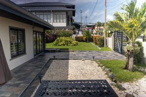 A residential property with a paved driveway, a small garden with various plants, and a metal gate.