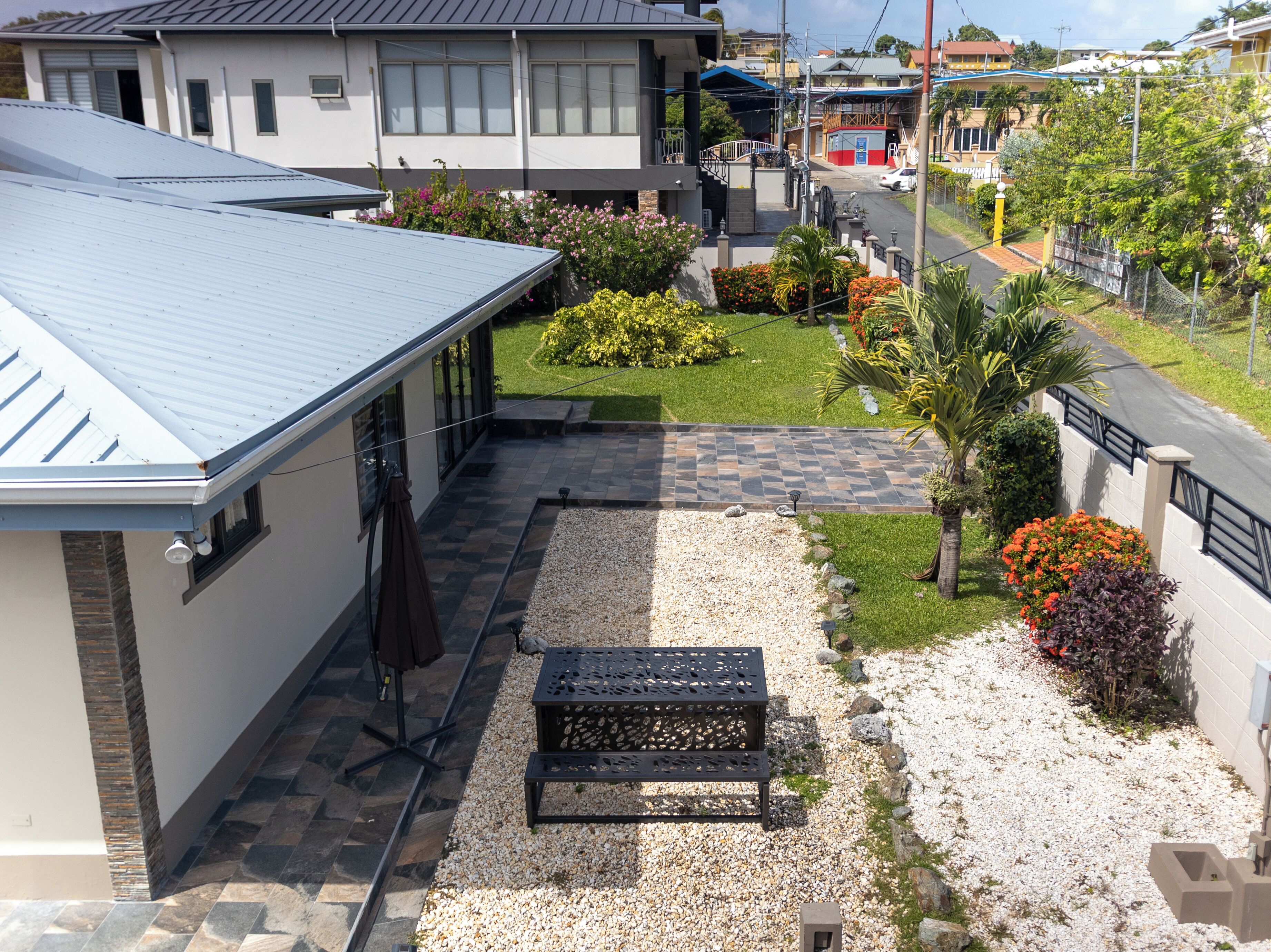 A residential property with a covered patio, a gravel pathway, and a small garden area with various plants and a bench.