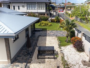 A residential property with a covered patio, a gravel pathway, and a small garden area with various plants and a bench.