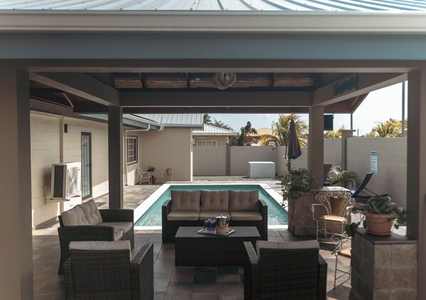 A covered outdoor area with a pool, seating, and potted plants.