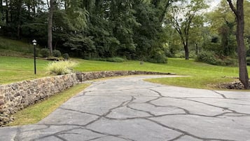 A paved driveway with a stone border, surrounded by grass and trees.
