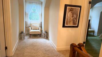 A hallway with a carpeted floor, a white chair, a framed picture on the wall, and a door leading to another room.