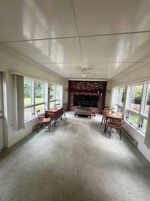 A room with a fireplace, a ceiling fan, and large windows.