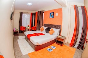 Une chambre d’hôtel comprenant un lit, une table de chevet, une chaise, une petite table et un téléviseur.