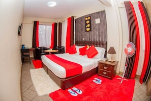 Une chambre d’hôtel avec un lit, une table de chevet, une lampe et un ventilateur.