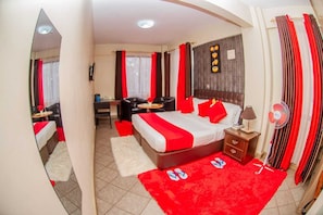 Une chambre d’hôtel avec un lit, un bureau, une chaise, un canapé, une moquette rouge et un miroir.