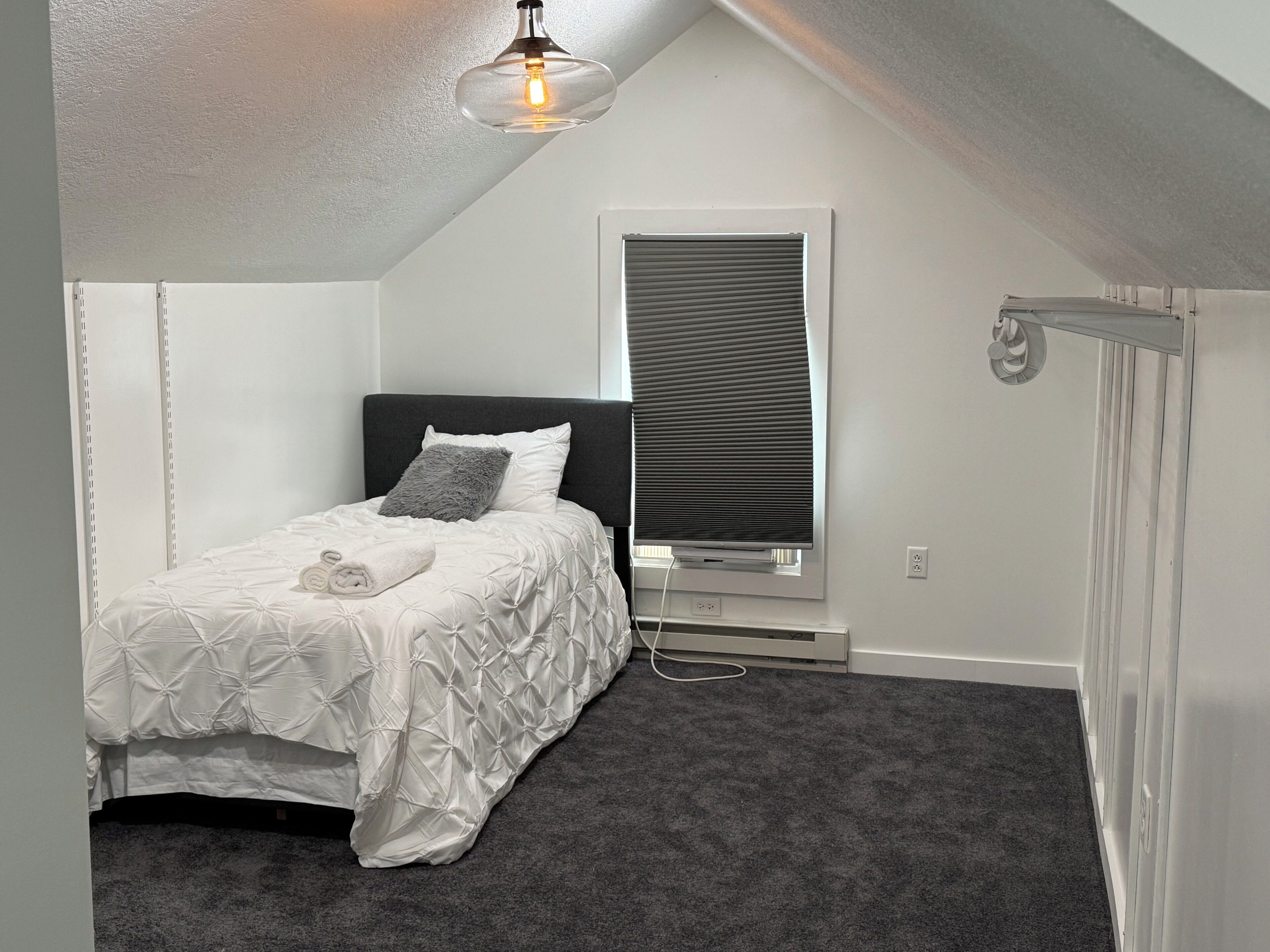 Een slaapkamer met een bed, een raam met zonwering, een plafondlamp en een radiator.