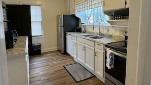 A kitchen with white cabinets, a black refrigerator, a sink, and a window with blinds.