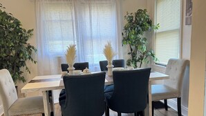 A dining area with a white table, dark chairs, and potted plants.