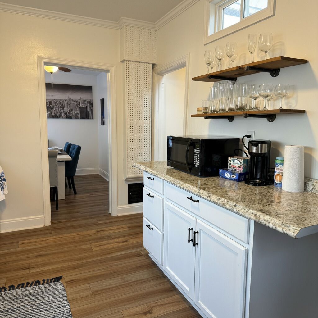 A kitchen with a microwave, coffee maker, and wine glasses on a shelf.