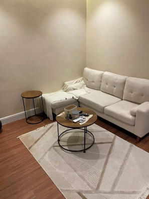 Ein Wohnzimmer mit einem beigefarbenen Sofa, einem runden Couchtisch, einem kleinen Beistelltisch und einem weißen Teppich.
