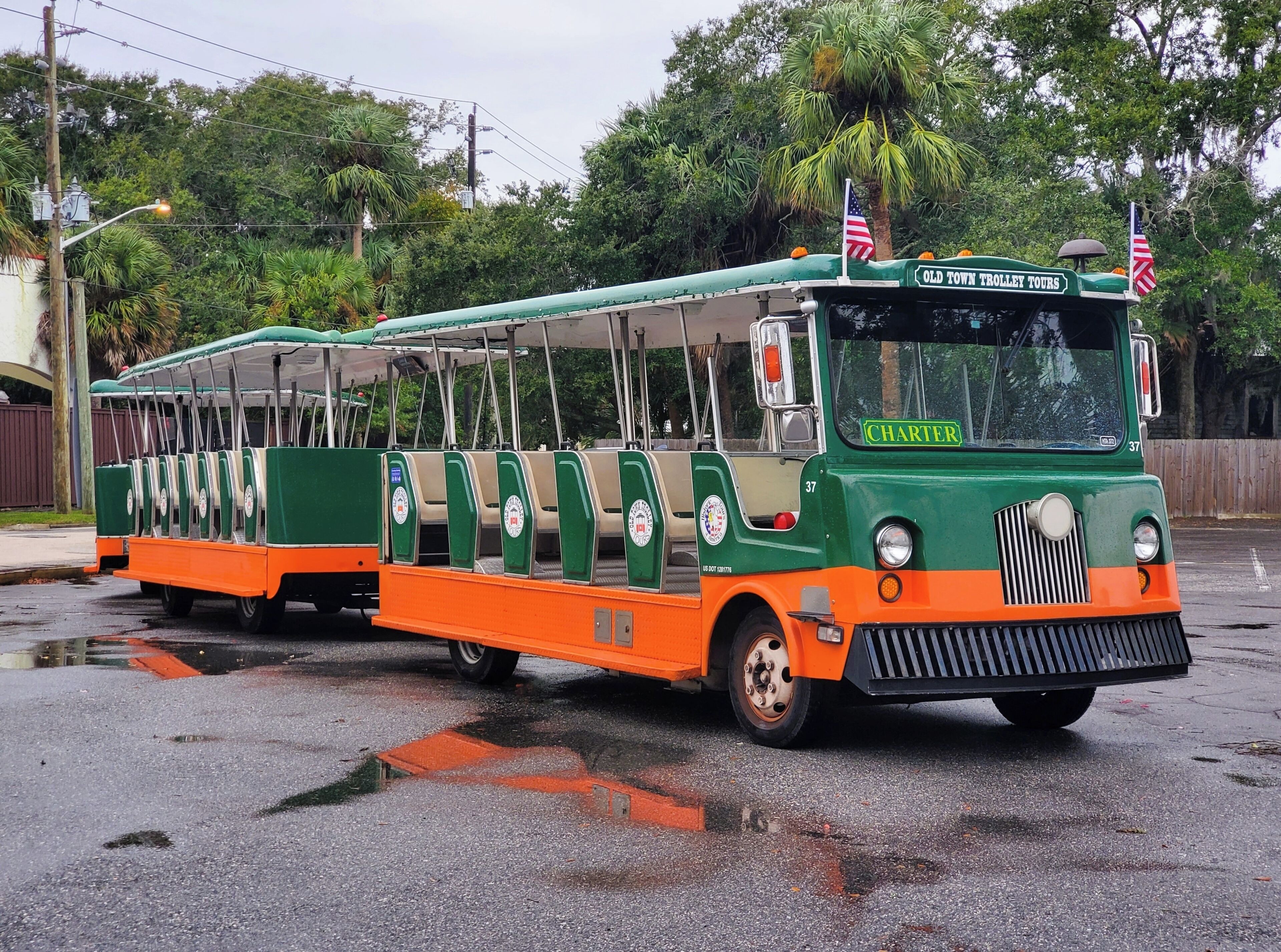 Vanhanaikainen, vihreän ja oranssin värinen raitiovaunu, jonka kylkeen on maalattu teksti »Old Town Trolley Tours», on pysäköity märälle kadulle.